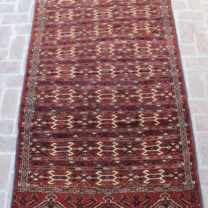 May include: A red, black, and cream colored rug with a geometric pattern. The rug has fringe on the ends.