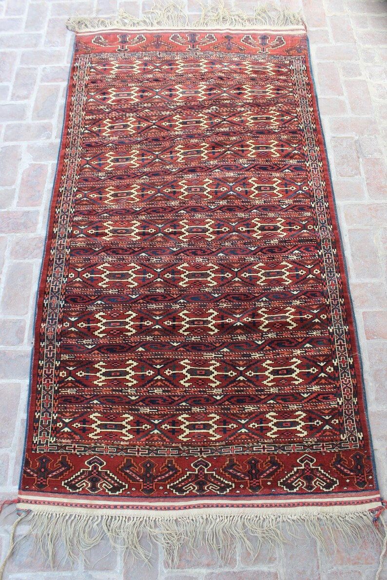 May include: A red, black, and cream colored rug with a geometric pattern. The rug has fringe on the ends.