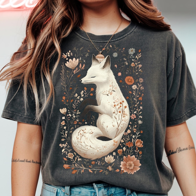 May include: Dark gray t-shirt featuring a white fox illustration surrounded by flowers. The fox has closed eyes and is adorned with floral details. The design includes various flowers in shades of brown, orange, and white.