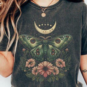 May include: A dark gray t-shirt with a green moth and floral design. The moth has a crescent moon on its back and the design includes a crescent moon with stars.