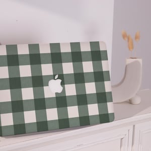 Può includere: Un computer portatile con un motivo a quadri verde e bianco sul coperchio. Il logo Apple è visibile sul coperchio.