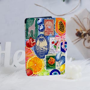 May include: A colorful collage of vintage stamps, fruits, and other designs. The stamps feature images of a bird, a palm tree, and a pineapple. The fruits include a papaya, a pomegranate, an orange, and a strawberry. The other designs include a seashell, a blue evil eye, and a pink bow.