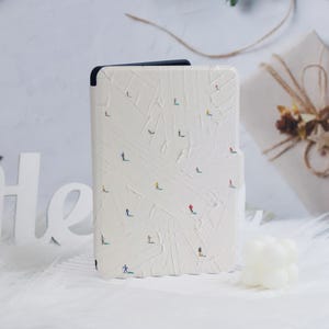 May include: A white e-reader cover with a pattern of skiers on a snowy mountain. The cover has a textured surface and a black border.
