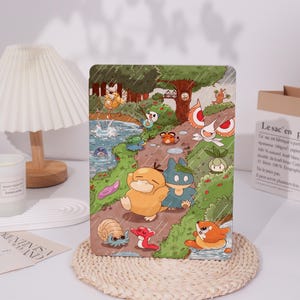 May include: A tablet case with a vibrant illustration of cartoon characters in a forest setting. The design includes various creatures, a path, and a rainy day scene. The case is rectangular and likely made from a robust material, suitable for protecting the device.