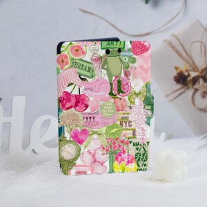 May include: A colorful case with a collage design featuring a frog, cherries, a cat, and the text "DREAM" and "ART!". The case has a mix of pink, green, and white elements, with a whimsical and artistic aesthetic.