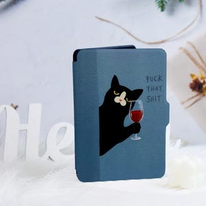 May include: A blue tablet case with a black cat illustration holding a glass of red wine. The text "FUCK THAT SHIT" is printed on the case. The cat has yellow eyes and a grumpy expression.