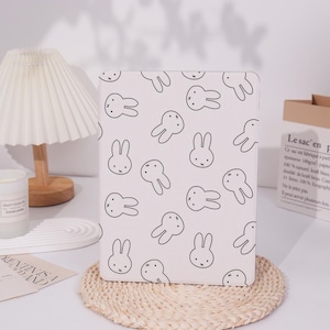 Peut inclure: Étui pour tablette blanc avec un motif de lapin blanc et noir. L'étui a un design simple avec un motif de lapins répété.