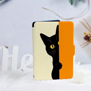 May include: A phone case featuring a black cat peeking out from behind an orange panel. The cat has yellow eyes and is set against a cream-colored background. The case is designed to protect the phone while adding a touch of whimsy.