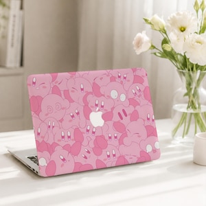 May include: A laptop computer featuring a protective skin cover with a repeating pattern of pink Kirby characters in various expressions. The center of the laptop lid displays a silver Apple logo cutout, surrounded by the dense graphic print of the character.