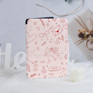 May include: A pink e-reader cover with a red and white pattern of hearts, arrows, cherries, cupcakes, and the word "LOVE".