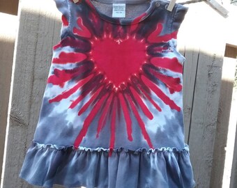 May include: A gray tie-dye baby dress with a red heart design. The dress has a ruffled hem and short sleeves.