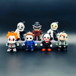 May include: A collection of seven small horror movie character figurines. The set includes figures resembling a clown with orange hair, a white and black clown, a striped sweater character with a hat, a blue jumpsuit figure, a puppet, and a hockey mask.