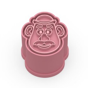 Op de afbeelding: Een roze plastic koekjessnijder in de vorm van een stripfiguurgezicht. De snijder heeft een hoed, ogen, een neus, een snor en een lachende mond. Ontworpen om koekjes of traktaties in de vorm van het personage te maken.