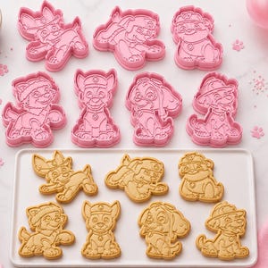 May include: A set of eight pink plastic cookie cutters shaped like various cartoon dog characters, accompanied by eight matching baked sugar cookies arranged on a white rectangular tray, featuring detailed embossed facial and clothing features.