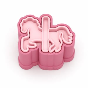 May include: A pink plastic cookie cutter shaped like a carousel horse. The design features a horse in a galloping pose with a vertical pole running through its centre, enclosed within a scalloped outer frame that defines the shape of the cutout.
