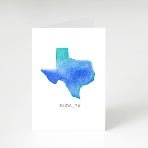 May include: A watercolor painting of the state of Texas in shades of blue and green. The text "BUDA, TX" is printed below the state outline.