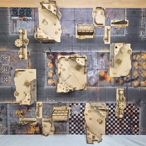 May include: A tabletop gaming terrain set featuring laser-cut light wood structures with jagged, ruined edges arranged on a printed mat. The mat displays a dark, weathered urban street layout with sections of gray pavement, checkered patterns, and debris.