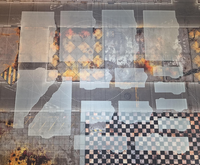 May include: A collection of translucent, rectangular acrylic templates arranged over a printed game mat featuring industrial, weathered textures, yellow hazard stripes, and a black and white checkered pattern across the surface.