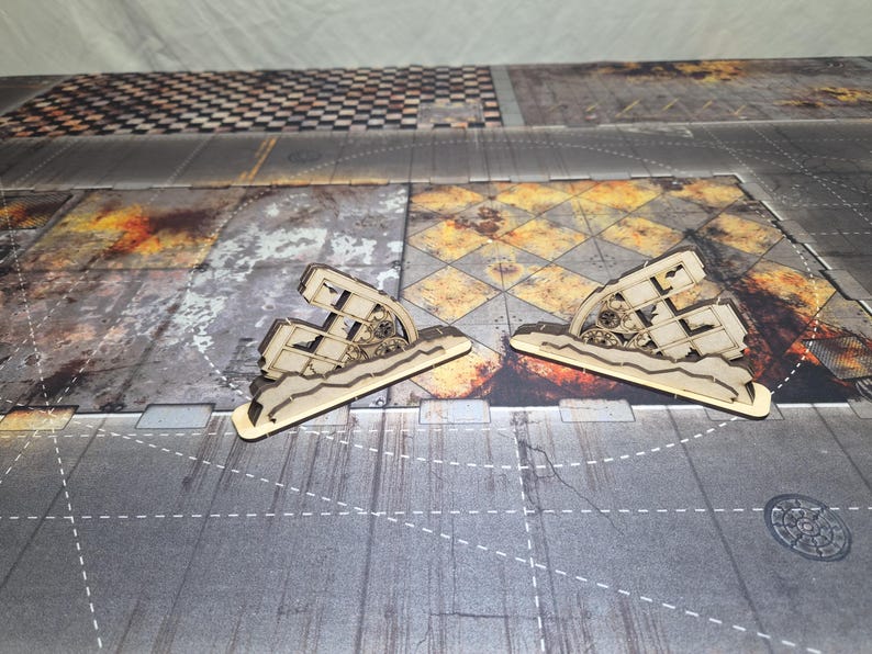 May include: Two light-colored laser-cut wooden terrain pieces featuring a jagged, ruined wall design with exposed gear-like mechanical details. These miniature structures are crafted from flat wood panels and stand upright on a textured base.