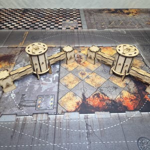 May include: A laser-cut wooden tabletop gaming terrain set featuring two cylindrical towers connected by modular bridge sections. The structures are made of light-colored plywood with engraved geometric details and triangular cutouts on the walls.