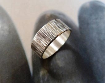 May include: A silver ring with a textured, ridged surface. The ring has a wide band and a polished interior. The ring is shown in a close-up shot, highlighting the detailed texture of the metal. The ring is a piece of jewelry.
