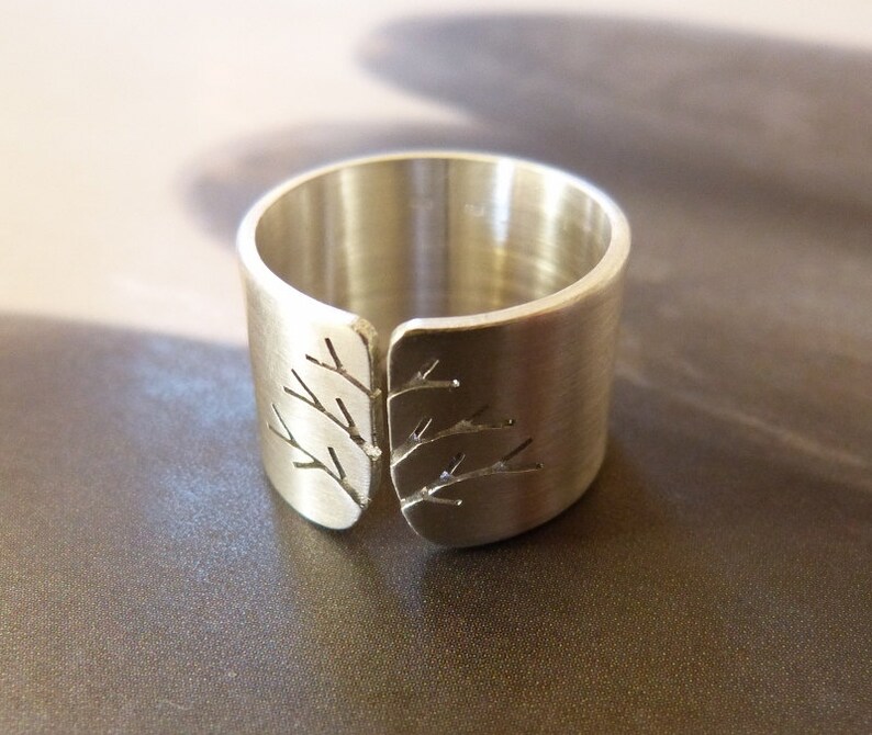 Pode incluir: Um anel prateado com um design de galho de &aacute;rvore. O anel tem um design aberto com um padr&atilde;o de galho de &aacute;rvore recortado na frente. O anel &eacute; feito de metal escovado.