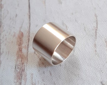 May include: A silver-colored ring with a cylindrical shape. The ring has a smooth, polished surface and a simple, minimalist design. The ring's diameter is approximately 1 inch.