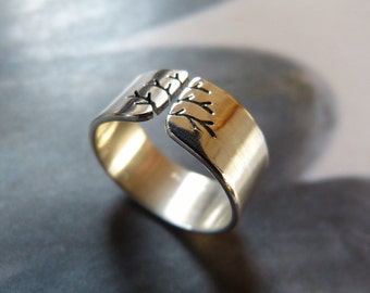 May include: A silver-toned ring with a split design. The ring features a brushed gold interior and a detailed tree branch pattern on the outer edges. The open design allows for adjustable sizing.