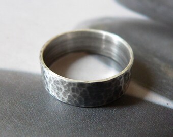 May include: A hammered silver ring with a textured surface. The ring has a wide band and a matte finish, reflecting light. The jewelry piece is likely made of sterling silver.