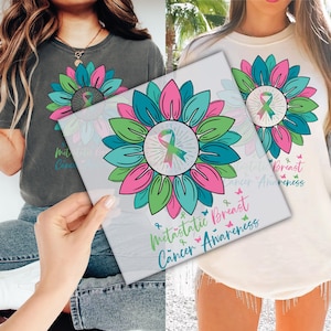 May include: A gray t-shirt and a cream-colored long-sleeve shirt, each featuring a colorful sunflower design with a ribbon in the center. The design includes the words "Metastatic Breast Cancer Awareness" in teal and pink.