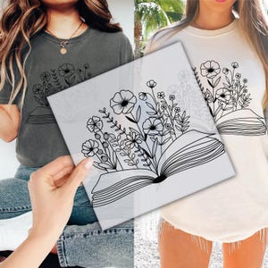 May include: A gray t-shirt and a cream-colored sweatshirt, each featuring a black line drawing of an open book with flowers and foliage sprouting from it. The design is centered on the front of the shirts, offering a botanical theme.
