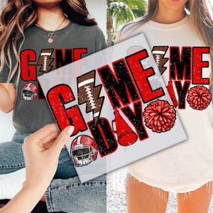 May include: Two t-shirts with the words "GAME DAY" in red and black distressed lettering. One shirt is gray, the other is cream. Football and helmet graphics are included in the design. The shirts are likely for football fans.
