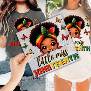 May include: Two t-shirts, one gray and one cream, featuring a graphic of a cartoon girl with a head wrap in the colors of the Pan-African flag. The text "little miss JUNETEENTH" is below the girl, with butterflies scattered around.