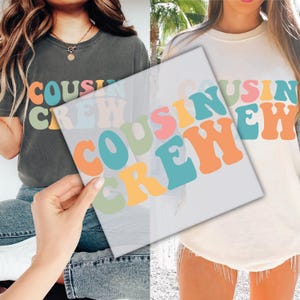May include: Two people wearing shirts with the text "COUSIN CREW" in colorful, retro-style letters. The shirts are a dark gray and a light cream color.