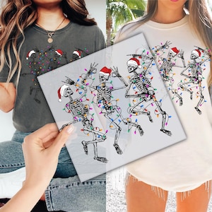 May include: A gray t-shirt and a cream-colored sweatshirt featuring a graphic of dancing skeletons wearing Santa hats and wrapped in colorful Christmas lights. The image is a festive holiday design.