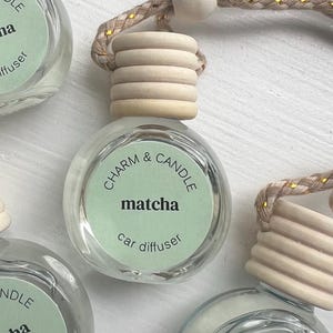 May include: A set of three glass car diffusers with a light green liquid and a wooden cap. The diffusers are labeled "CHARM & CANDLE matcha car diffuser".