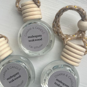 May include: Three glass car diffusers with wooden stoppers and rope hangers. Each diffuser has a label that reads "CHARM & CANDLE mahogany teakwood car diffuser".