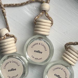 May include: Three glass car diffusers with a white label that says "CHARM & CANDLE coffee car diffuser". The diffusers are hanging from a string with a wooden bead.