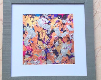 May include: Abstract painting in a gray frame. The painting features a mix of gold, silver, pink, purple, and blue paint splatters.