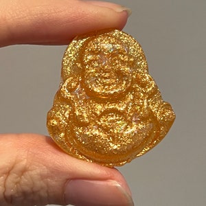 May include: A gold-colored resin figurine of a smiling Buddha, with a glittery finish.