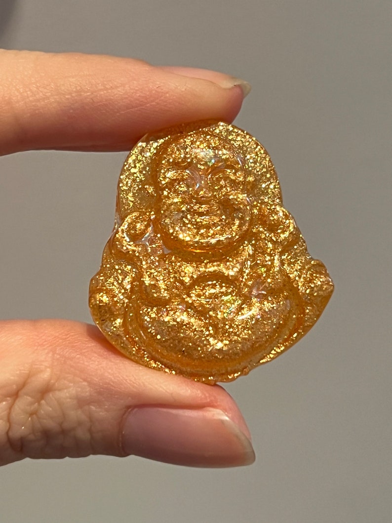 May include: A gold-colored resin figurine of a smiling Buddha, with a glittery finish.