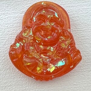 May include: Orange glass pendant with a smiling Buddha figure. The pendant has a iridescent finish.