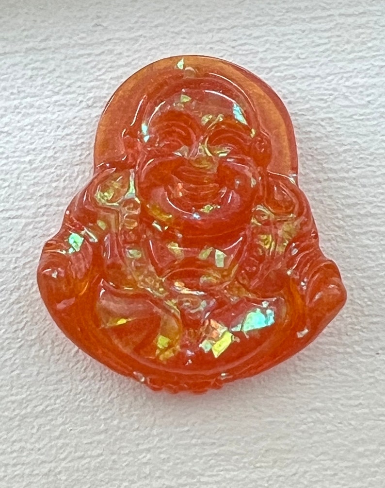 May include: Orange glass pendant with a smiling Buddha figure. The pendant has a iridescent finish.