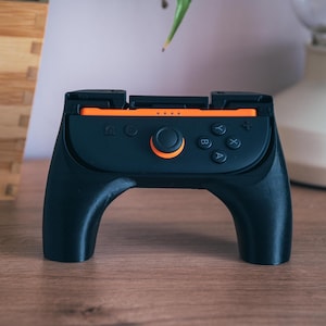 K&ouml;nnte beinhalten: Eine wei&szlig;e Keramik-Tasse mit schwarzem Henkel und dem Text "But First, Coffee" in schwarzer, handschriftlicher Schrift. Die Tasse steht auf einer wei&szlig;en Oberfl&auml;che.