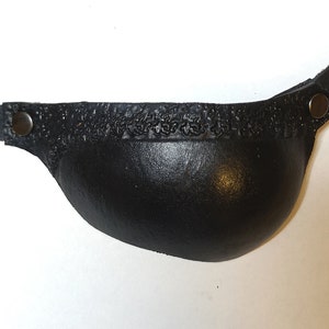 Puede incluir: Un parche para el ojo de cuero negro con una correa y dos broches metálicos. El parche está diseñado para cubrir un ojo.