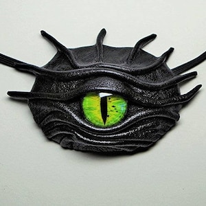 Könnte beinhalten: Ein schwarzes Leder-Augenpflaster mit einem grünen Auge. Das Augenpflaster ist so gestaltet, dass es wie ein Monsterauge aussieht.