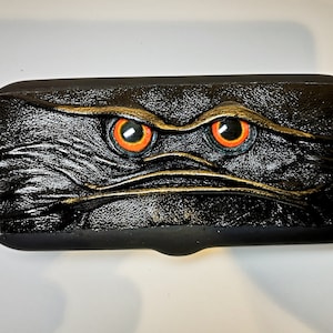 May include: Black leather eyeglasses case with a textured surface and two orange eyes.