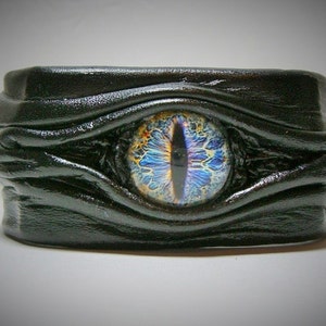 May include: Black leather bracelet with a blue and gold eye design.