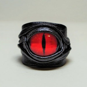 Peut inclure: Une bague en cuir noir avec un motif d'&oelig;il rouge. La bague est en cuir et a un &oelig;il rouge au centre.