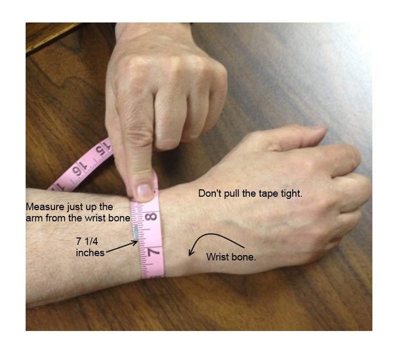 Puede incluir: Una cinta m&eacute;trica rosa est&aacute; envuelta alrededor de la mu&ntilde;eca de una persona. La cinta m&eacute;trica indica 7 1/4 pulgadas. El texto en la imagen dice "Mida justo arriba del brazo desde el hueso de la mu&ntilde;eca" y "No tire de la cinta demasiado fuerte." Una flecha apunta al hueso de la mu&ntilde;eca.